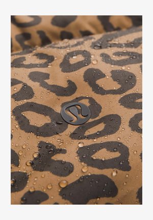 Wasserabweisender Stoff mit beige Hintergrund und einem schwarzen Leopardenmuster. Kleine Tropfen sind auf der Oberfläche sichtbar. Logo-Detail vorhanden.