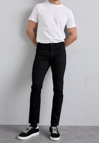 Svart slim-fit jeans med en klassisk femficksdesign, i kombination med en enkel vit kortärmad t-shirt och svarta sneakers.