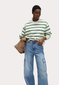 Grönrandig tröja med krämfärgad bas, tillsammans med ljusblå baggy jeans med cargofickor. Håller en brun vävd clutchtv.