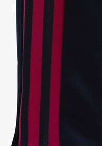 Prenda atlética en color navy con dos franjas rojas verticales. La tela es texturizada, con un patrón de malla en las franjas para mayor transpirabilidad.