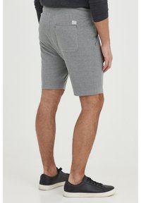 Pantalones cortos de algodón gris con un acabado texturizado, que presentan un bolsillo en la parte posterior y un sutil acento de logo. Combinados con zapatillas negras.