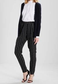 Svart och vitrandiga byxor med hög midja, i kombination med en vit blus och en marinblå kavaj, med slim fit-design och ankle-längd.