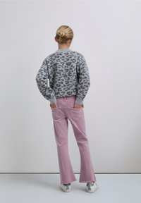 Jersey gris con estampado de leopardo, vaqueros rosados acampanados con dobladillos deshilachados y zapatillas blancas con detalles plateados. Visto de espaldas sobre un fondo liso.