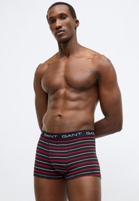 Fekete és piros csíkos boxeralsó fekete derékrésszel, amelyen fehér betűkkel szerepel a "GANT" márkanév. Simább anyagból, testhezálló kialakításban.