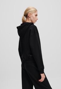 Zwarte hoodie met een relaxte pasvorm, gemaakt van zachte stof. Heeft een verlengde schouderlijn en ribgebreide manchetten. Eenvoudig, minimalistisch ontwerp.