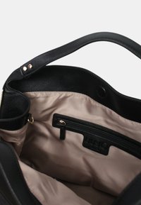 Bolso de mano de cuero negro con un exterior suave, un forro de tela beige y un bolsillo interior con cremallera. Presenta detalles en hardware dorado y una correa de hombro.