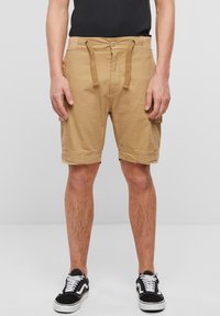 Khakifargede cargoshorts med snøring og knappelukking, sidelommer og en avslappet passform, kombinert med svarte joggesko.