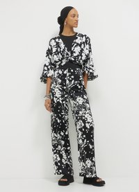 Kimono in bianco e nero con motivo floreale e maniche a campana, abbinato a pantaloni a vita alta e gamba larga. Sandali con tacco blocco neri.