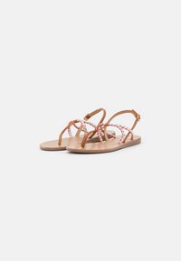 Tan leather sandals with braided red and white straps, flat sole, open toe design, and adjustable ankle buckle closure.