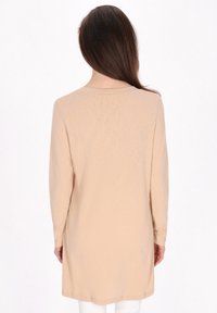 Top beige a maniche lunghe, in tessuto morbido, con scollatura rotonda e taglio dritto. La vista posteriore mostra una texture liscia e un design minimale.