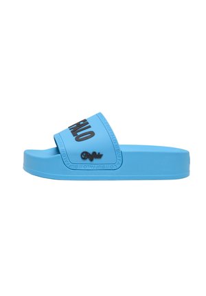 Persona che indossa sandali platform slip-on blu brillante del marchio Buffalo, in piedi su un marciapiede in cemento chiaro all'aperto.