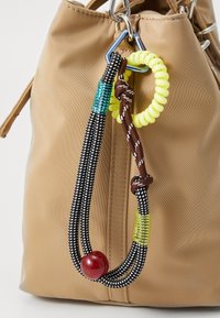 Borsa marrone chiaro con un portachiavi colorato. Il portachiavi presenta cordini neri e marroni, una spirale gialla, accenti turchesi e una perla rossa.