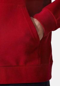 Sudadera roja con capucha que cuenta con un bolsillo tipo canguro en la parte frontal, puños y dobladillo acanalados, y una textura suave. El diseño prioriza la comodidad y la funcionalidad.