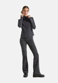 Zwarte lange mouwen turtleneck shirt met een ontspannen pasvorm, gecombineerd met zwarte flared broek en zwarte sneakers, tegen een witte achtergrond.