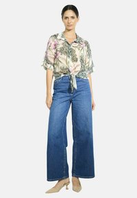 Floral patterned, short-sleeve, light-colored shirt with a tie at the waist; paired with wide-leg blue denim jeans and nude heels.