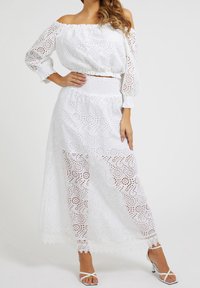 Witte off-the-shoulder top en maxi rok set met oogjesontwerp, smocktail en kantafwerking, gecombineerd met witte enkelbandjes.