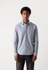 Férfi kék és fehér csíkos ing, gombos gallérral, texturált anyagból, hosszú ujjakkal és mellzsebbel. Feszes sziluettre tervezve.