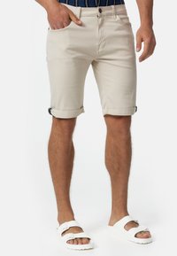 Beżowe bawełniane szorty z podwiniętymi brzegami, przednimi kieszeniami i zapięciem na guzik. Noszone z białymi sandałami. Minimalistyczny design, jednolity kolor.