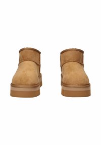 Un paio di stivali alla caviglia in camoscio beige con suole spesse e cuciture visibili, mostrati frontalmente su uno sfondo bianco.