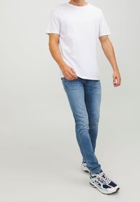 Camiseta blanca de manga corta combinada con jeans azul claro y zapatillas deportivas con acentos en azul, blanco y marino.