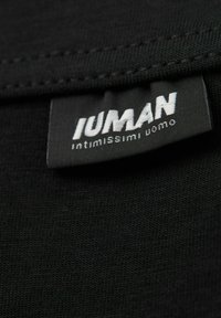 Svart tygmärke med vit text som läser "IUMAN" och "intimissimi uomo." Texturen och sömmarna är synliga.