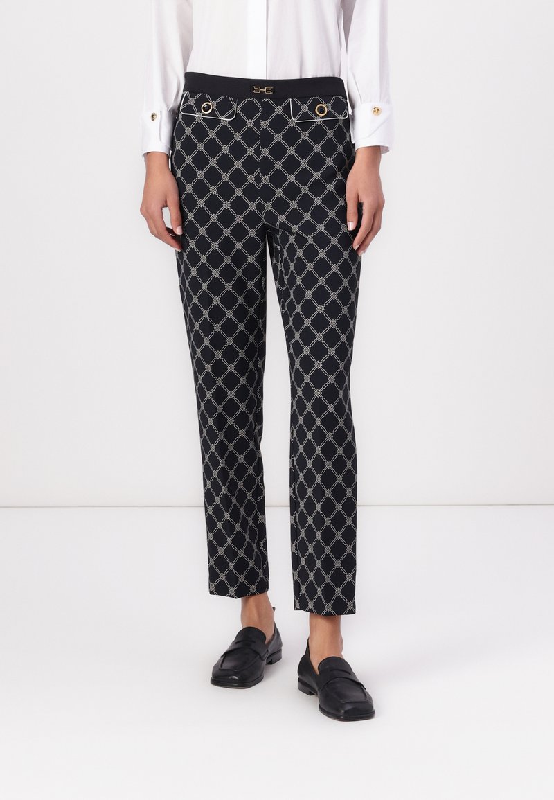 Black patterned trousers featuring a geometric design, gold hardware accents, and a fitted waist with side pockets. Smooth fabric texture.