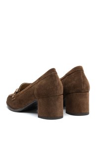 Ett par bruna mocka blockklackarna loafers med guldbuckledetalj, visade från bakre högra sidan på vit bakgrund.