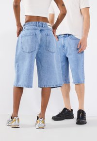 Light blue denim shorts with a relaxed fit, five pockets, and frayed hems, worn with silver and black athletic shoes.