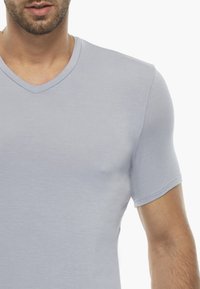 T-shirt grigio chiaro a maniche corte con scollatura a V, realizzato in un tessuto morbido e liscio. La vestibilità è aderente, enfatizzando una silhouette pulita.
