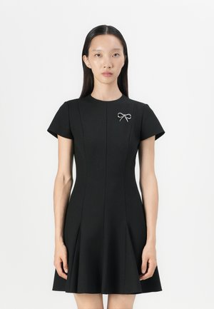 Black A-line dress with short sleeves, a fitted bodice, and a slight flare. Features a small silver bow brooch accent on the left.