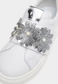 Vit lädersneaker med silvermetalliska accenter, utrustad med två stora glittriga blommönster-applikationer och en liten pärldetalj på remmen.