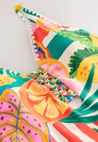 Tissu de maillot de bain coloré avec des motifs de fruits tropicaux et de feuilles, comportant un détail circulaire tressé au centre.