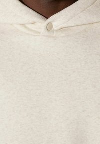 Krämfärgad hoodie i ett mjukt texturerat tyg, med en framträdande knapp vid halsen och en klassisk huva.