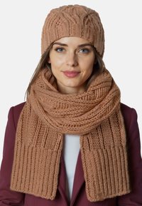 Strikket tørklæde og hue sæt i rose beige. Tørklædet har en ribbet tekstur, mens huen har et forhøjet kabelmønster. Begge er lavet af blødt garn.