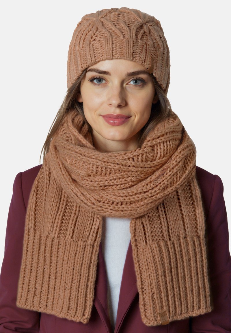Strikket tørklæde og hue sæt i rose beige. Tørklædet har en ribbet tekstur, mens huen har et forhøjet kabelmønster. Begge er lavet af blødt garn.