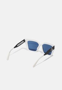 Lunettes de soleil blanches angulaires avec des verres bleus. Présentent une monture noire avec des accents de logo et des embouts blancs. Fabriquées en plastique avec une finition mate.