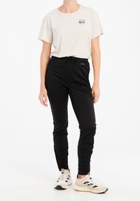 Jasnobeżowa koszulka z krótkim rękawem z małą, wielokolorową grafiką, zestawiona z czarnymi dresami z elastycznym pasem i sznurkiem do regulacji.