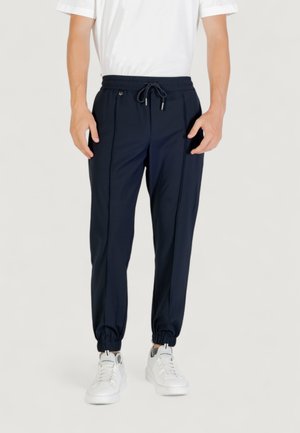 Pantaloni jogger traspiranti di colore navy con vita elastica, cordino regolabile e polsini affusolati. Abbinati a sneaker bianche.