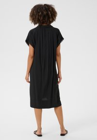 Black knee-length dress with short, lace-trimmed sleeves. Features a relaxed fit and a back pleat for movement. Smooth fabric texture.