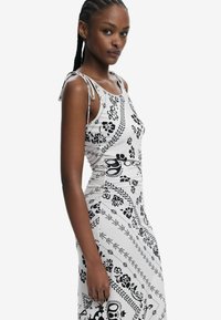 Schwarz-weißes Kleid mit Blumendesign, figurbetonter Silhouette, ärmellosem Schnitt und verstellbaren Bindebändern. Glattes Material mit leichtem Glanz.