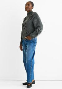 Maglione grigio lavorato a maglia con dettagli in rilievo a pom-pom, abbinato a jeans blu a gamba dritta e scarpe nere basse. Design semplice e moderno.