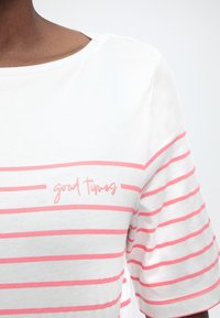 Λευκό πουκάμισο με ροζ οριζόντιες ρίγες και το κέντημα "καλές στιγμές" σε ροζ στο στήθος, φορεμένο από άτομο με σκούρο δέρμα.