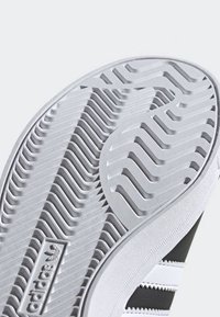 Podeszwa czarno-białego buta marki Adidas z wzorzystym bieżnikiem i logo oraz część cholewki z białymi paskami na czarnym tle.