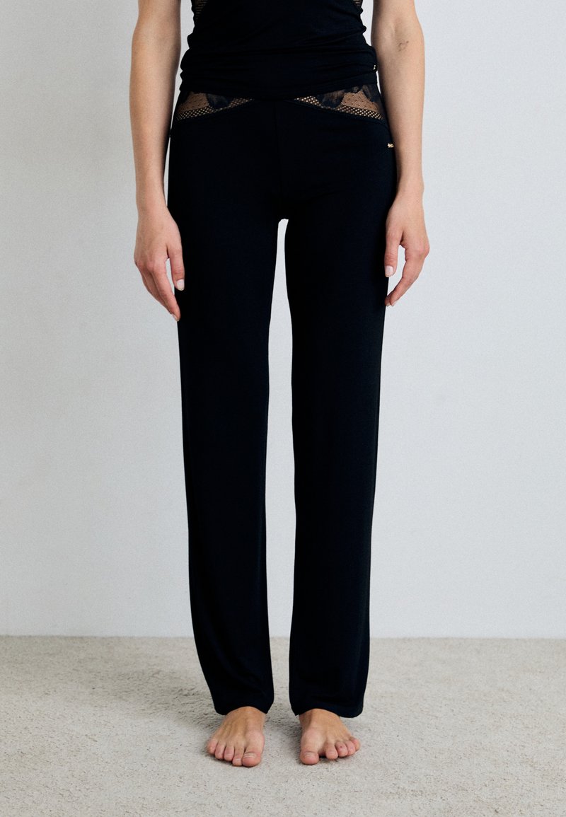 Musta, istuva housut, joissa on sileä pinta ja läpinäkyvä pitsipaneeli vyötäröllä. Suunniteltu mukavuutta ja joustavuutta varten, nilkkapituus.