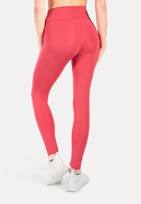 Leggings rosa a vita alta, aderenti, realizzati in tessuto elasticizzato; indossati con scarpe da ginnastica bianche. Tessuto liscio, senza motivi visibili.
