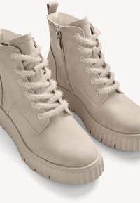 Beige Ankle Boots aus weichem Leder, mit einem strukturierten, flauschigen Schnürdetail, einem seitlichen Reißverschluss und einer derben, profilierten Sohle.