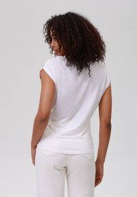 Hvit kortermet topp med en jevn tekstur, med rund hals og en tettsittende design, kombinert med kremfargede bukser.