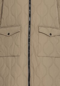 Beige gesteppte Jacke mit Reißverschluss vorne, zwei Klappentaschen und einer Wellenmuster-Oberfläche. Verfügt über einen schwarzen Reißverschluss und Akzente.