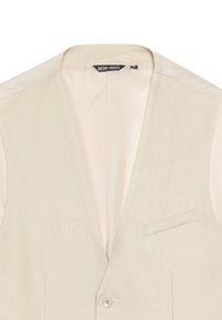 Gilet in lino beige con scollatura a V profonda, chiusura con un bottone e tasca laterale. L'interno presenta una leggera fodera, etichetta visibile sul collo.