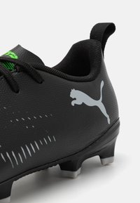 Musti jalkapalloiluun musta, jossa on teksturoitu pinta, vihreät yksityiskohdat ja näkyvä harmaa Puma-logo. Varustettu matalalla leikalla ja muotoilluilla napeilla pidon parantamiseksi.